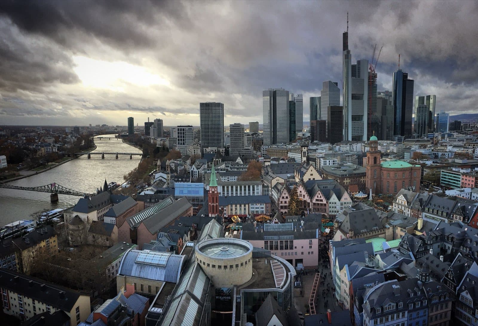 Skyline des Frankfurter Bankenviertels mit Main und Altstadt unter dramatischem Himmel — Zentrum des DACH-Finanzdistrikts und Heimat eines Großteils der hiesigen PE- und M&A-Aktivität.