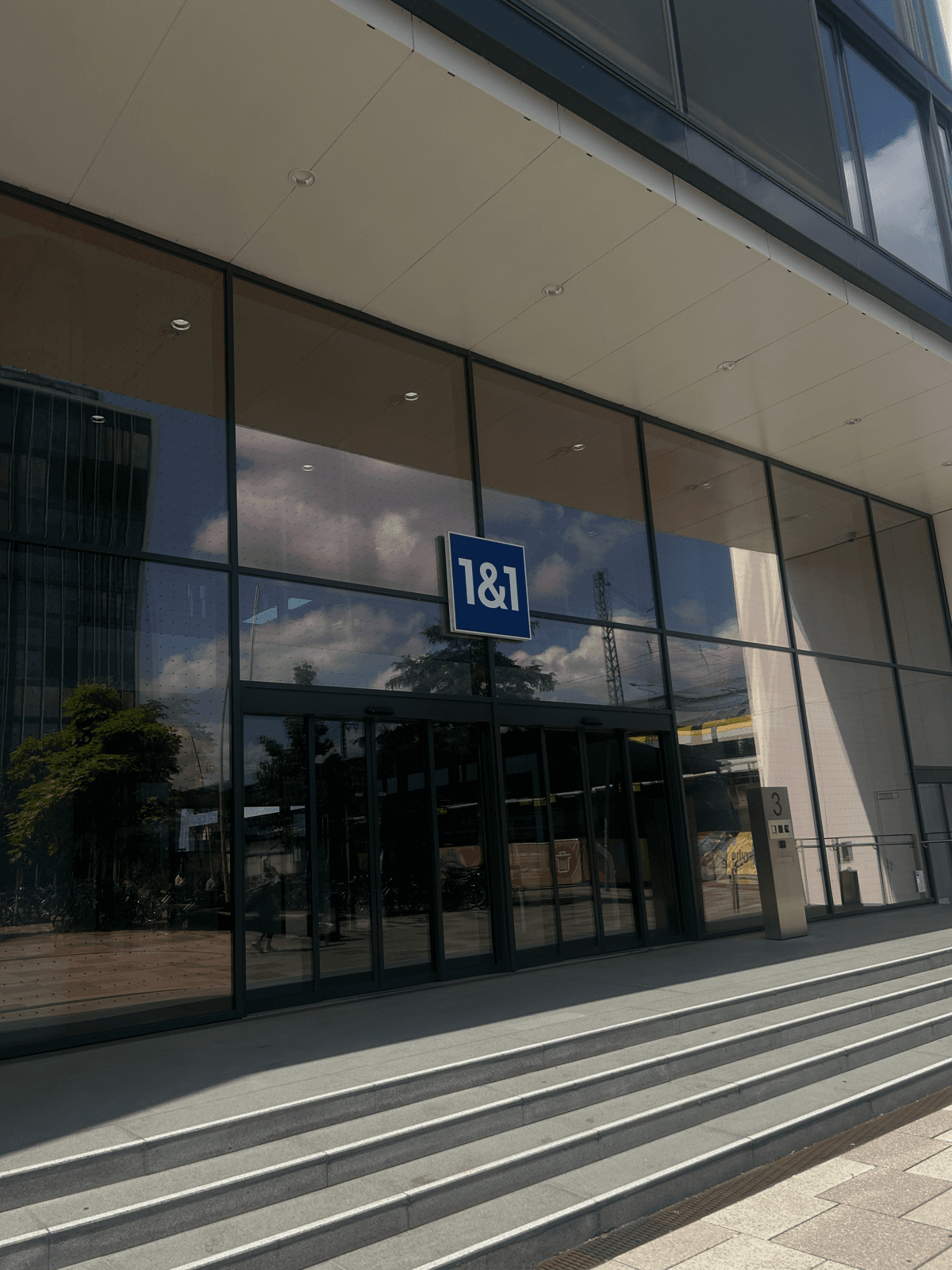 Glasfassade mit blauem 1&1 Logo — Standort von 1&1 in Deutschland, gesehen von der Straße aus.