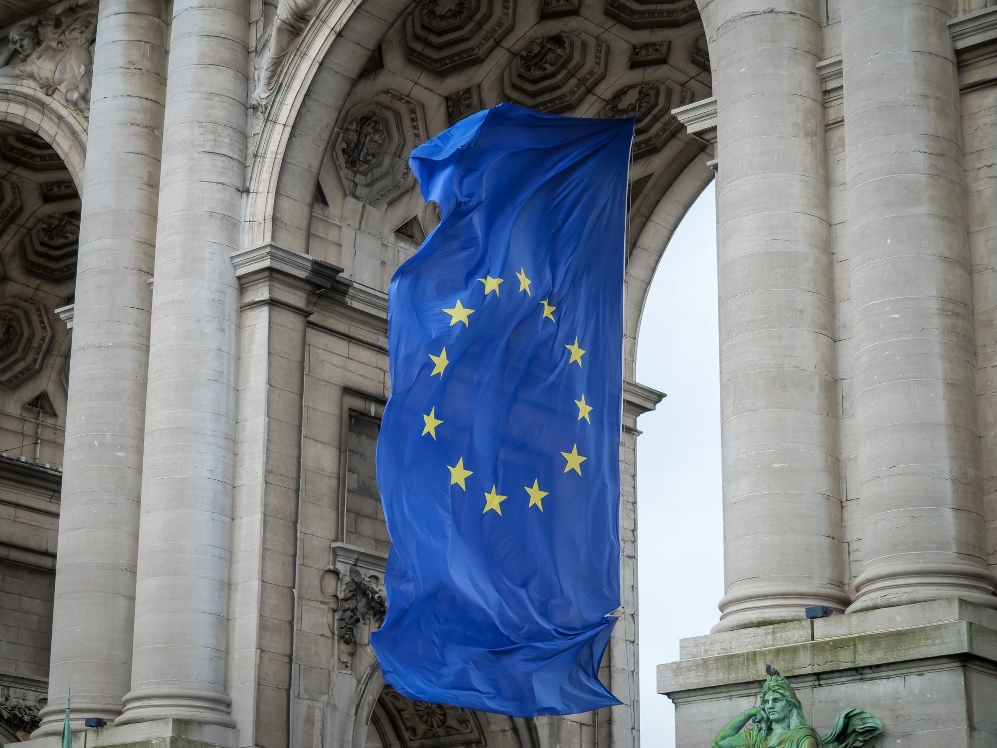 The flag of the European Union with twelve golden stars flying beneath the Cinquantenaire arch in Brussels